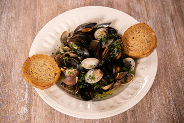 Food photography. Plate with mussels in wine sauce, close up view against a wooden table. Delicious seafood.