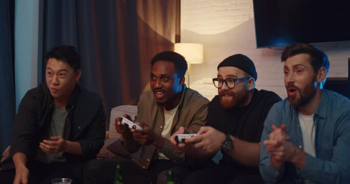 Happy Male Friends bring Drinks for Friends and start Playing Video Games. Holding Joystick and using PlayStation Having Fun while sitting at Home and Resting. Men Party. Students. Cheering. Goal.