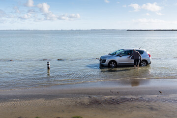 Voiture les roues dans la mer illustrant la montée des eaux liée au réchauffement climatique global, le chauffeur récupérant son véhicule les pieds dans l'eau.