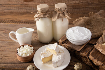 fresh dairy products for daily consumption. two bottles of milk, a bowl of sour cream and cottage cheese on a wooden table.