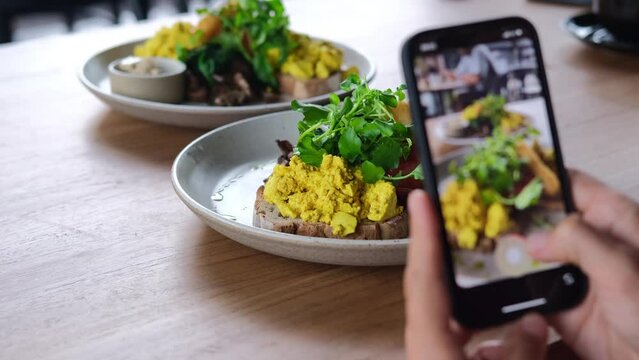 Lifestyle blogger tacking videos and photos of fresh morning toasts with scrambled eggs for social media content in a cafe
