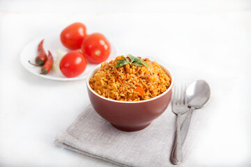 Jollof rice with parsley in a ceramic cup tomatoes and peppers on a linen napkin on a white background. National cuisine of Africa.