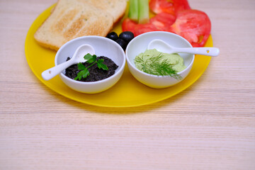 Close up of healthy breakfast with toasts, avocado dip, olive paste, tomatoes and cucumbers