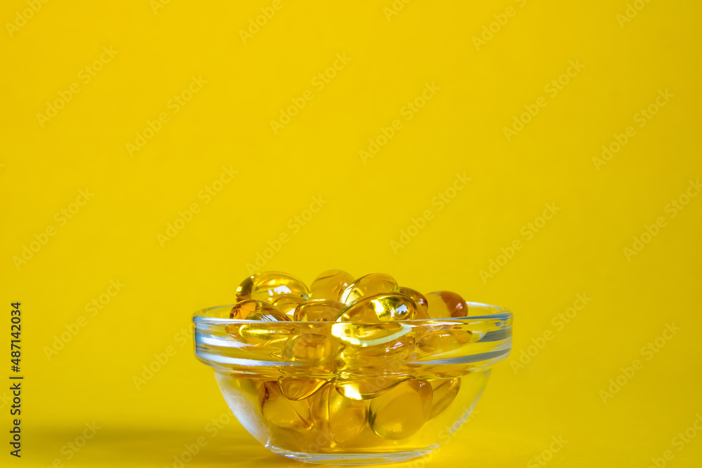 Wall mural bowl with omega 3 capsules on yellow background with copyspace, side view