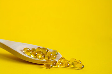 wooden spoon with omega 3 capsules on yellow background, copyspace, healthy lifestyle