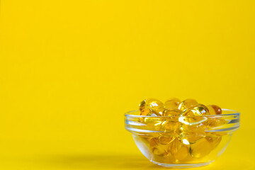 bowl with omega 3 capsules on yellow background with copyspace, side view
