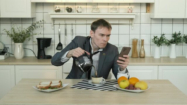 Young Businessman in Suit Pouring Morning Coffee and Using Smartphone while Having Breakfast at Home. Coffee Spills over the Rim of Cup. Loopable Cinemagraph Video, Motion Photo