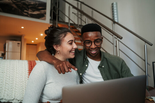 African American male with caucasian girlfriend typing on laptop while sitting on couch