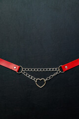 Silver metal chain and red leather choker with heart symbol on black background 