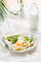 Traditional breakfast. Crepes with eggs, cheese and avocado. Traditional dish galette sarrasin on a vintage green plate.
