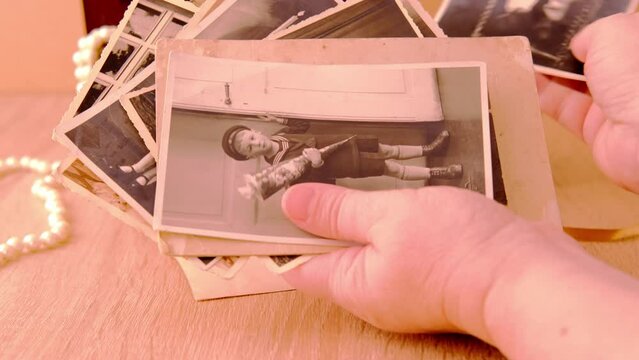 close-up female hand holding old vintage photos in sepia color 50s, 60s, carefully sorts out family values, concept of family tree, genealogy, memory of ancestors, family ties, childhood memories