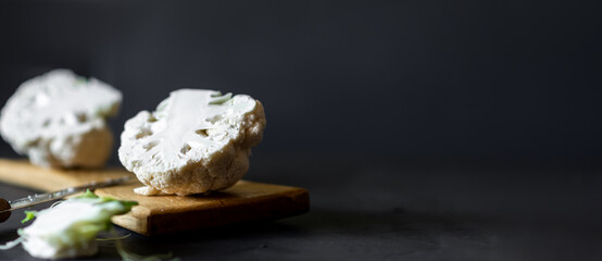 Cauliflower on a wooden cutting board. Dark background. Place for text. Side view.