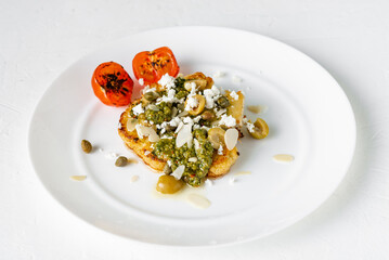 Cauliflower steak with spices, chimichurri sauce, almond flakes, olives, fried cherry tomatoes and capers on a white plate. Vegetarian food.