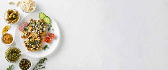 Vegetarian food concept. Cauliflower steak with spices, chimichurri sauce, almond flakes, olives, fried cherry tomatoes and capers on a white plate. White background. Banner, place for text.