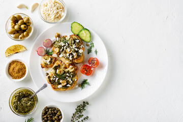 Vegetarian food concept. Cauliflower steak with spices, chimichurri sauce, almond flakes, olives, fried cherry tomatoes and capers on a white plate. White background.