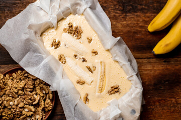Banana bread. Cooking. Raw dough with banana and walnuts in a baking dish. Wooden background. Sweet, vegetarian food.