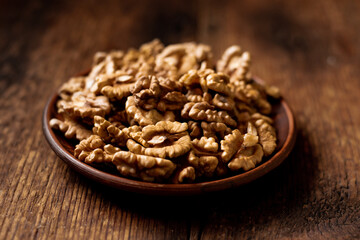 Obraz premium Peeled walnuts on a plate. Dark wooden background. Vegetarian, healthy food.