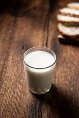 A full glass of milk. Bread in the background is blurred. Dark wooden background. Morning breakfast. Healthy food. Vertical frame.