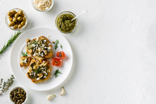 Cauliflower steak with spices, chimichurri sauce, almond flakes, olives, fried cherry tomatoes and capers on a white plate. Vegetarian food. White background. Copyspace.