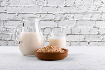 Vegan non diary buckwheat milk in jug and glass with buckwheat groats a bowl on a white stone table. Vegan buckwheat drink is plant based alternative milk . Veggies healthy milk product in pitcher