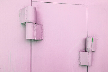 Close-up of metal hinges on the gates of a metal garage, painted pink, outdoors