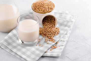 Vegan non diary buckwheat milk in glass with buckwheat groats in a bowl and on white stone table. Vegan buckwheat drink is plant based alternative milk . Veggies healthy milk product, selective focus