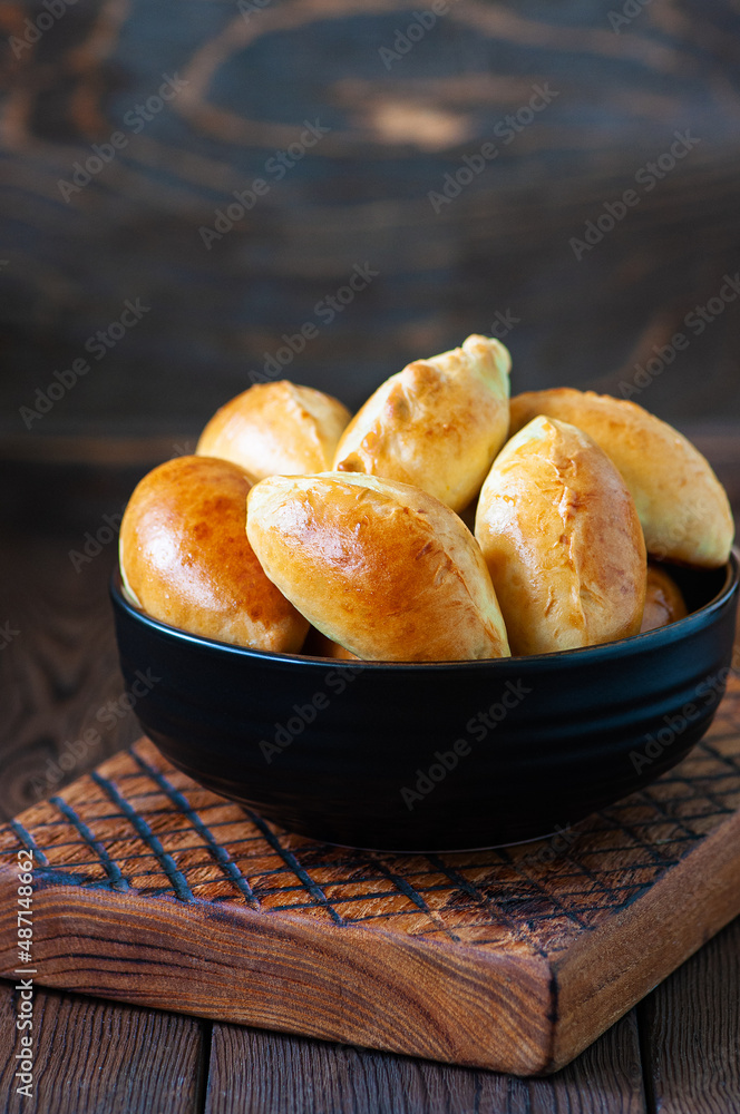 Wall mural Potato stuffed hand pies in a black bowl on a wooden board.