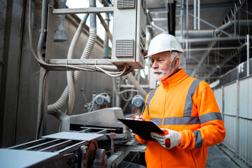 Industrial worker supervisor standing by machine and checking production in manufacturing factory.