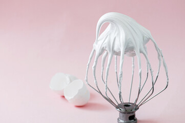 Whipped egg whites - beaten italian meringue on a wire whisk and egg shells on pink background. - 487148695