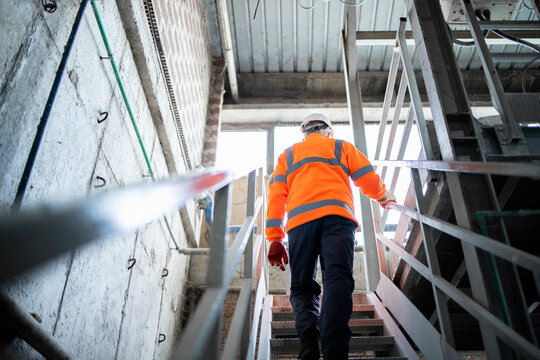 Industrial worker engineer in safety equipment and hard hat climbing metal staircase in factory.