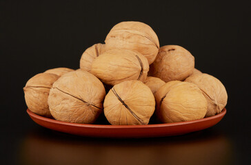 A mound of walnuts on a clay plate on a black background