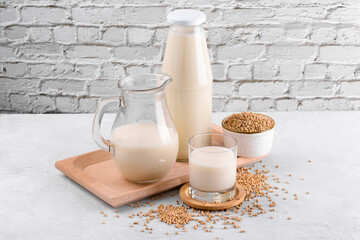 Vegan non diary buckwheat milk in bottle, in jug and glass with buckwheat groats in a bowl and on white stone table. Vegan buckwheat drink is plant based alternative milk. Veggies healthy milk product