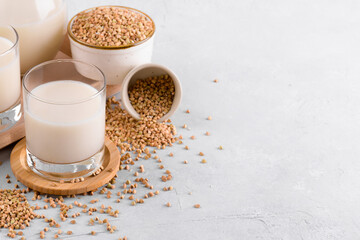 Vegan non diary buckwheat milk in glasses with buckwheat groats in a bowl on white stone table. Vegan buckwheat drink is plant based alternative milk . Veggies healthy milk product, copy space