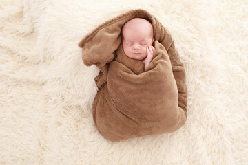 
7 day old baby sleeps happily in bed on a white fluffy blanket wrapped in a fluffy brown blanket in a white room