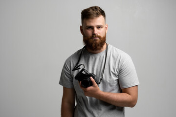 Portrait of bearded professional photographer with dslr camera looks straight into the camera isolated on gray background.