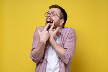 Man in glasses and casual clothes opened his mouth and shows a missing tooth with fingers. 