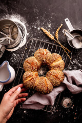 Baking breadstuff - gold bread roll (bagel) with sesame in baker’s hand on black