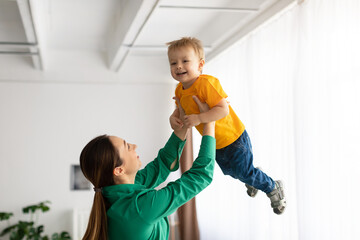 Motherhood concept. Playful lady holding her smiling child boy, lifting son high up in the air,...
