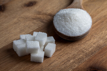 Granulated sugar and sugar cubes in wooden spoon on wooden background