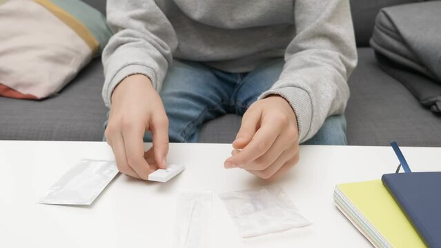 Teenage boy hands unpacking Covid-19 rapid antigen self test kit at home. Kid preparing test kit to self-test before school lesson