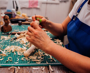 A female carpenter cuts wood with a knife in a carpentry or makeshift workshop. Dust and shavings...