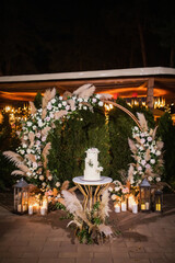 night wedding ceremony, the arch is decorated with flowers, candles and garlands of light bulbs and there is a wedding cake on the table