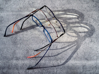 The eyeglasses are placed next to each other. The shadow from the glasses and the light passing through the lenses are visible on the table surface. Background with glasses to improve vision.