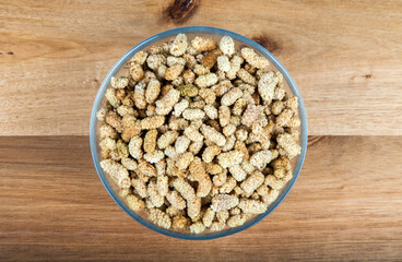 Dried mulberry in glass bowl on wooden background