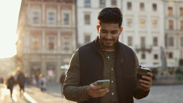 Indian guy walking on street with coffee and mobile