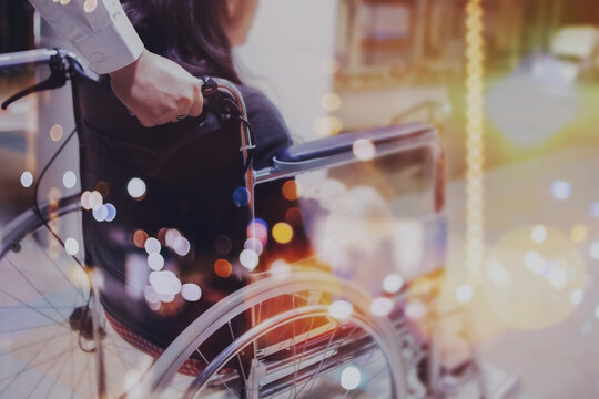 blurred of a man hand helping elderly woman on wheelchair outdoor  on the footpath in the night with Bokeh light, copy space
