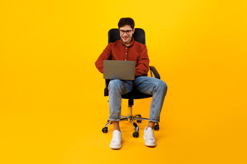 Man Using Laptop Computer Sitting In Chair Over Yellow Background