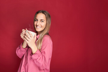 Young woman smiling while drinking a cup of hot chocolate. Isolated on red background
