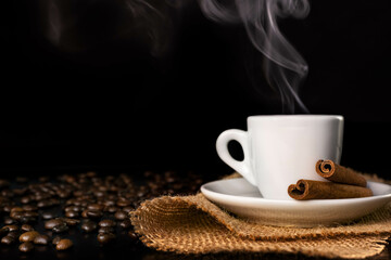 Cup of coffee on burlap with cinnamon and smoke and coffee beans on a dark background