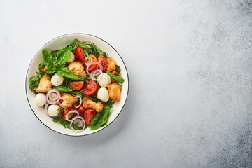 Panzanella Bread Salad. Traditional food of Italy with tomatoes, mozzarella balls, basil, onion and bread on light grey background. Traditional Italian cooking. Top view. Copy space.